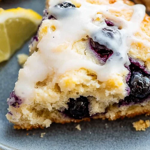 Blueberry Lemon Scone Recipe: Buttery and Perfect for Brunch 2 Close-up of a blueberry lemon scone slice with lemon glaze and a fresh lemon wedge on a blue plate.