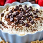 Creamy cannoli dip topped with chocolate chips and cocoa powder, surrounded by strawberries, chocolate, and waffle cookies.