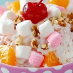Ambrosia salad with mandarin oranges, maraschino cherries, mini marshmallows, and chopped walnuts in a polka dot bowl.