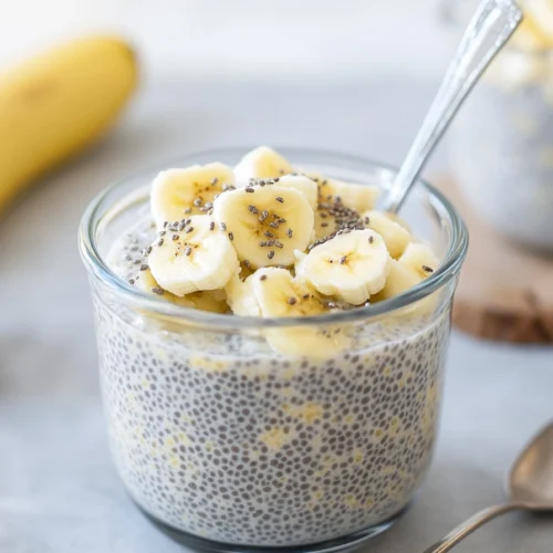 Overnight Paleo Oats: The Best Healthy Make-Ahead Breakfast Without Oats 2 Glass jar filled with banana chia pudding topped with sliced bananas and chia seeds, with a spoon inside.