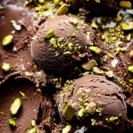 Close-up of rich Dubai chocolate ice cream with crushed pistachios and coconut flakes in a metal container.
