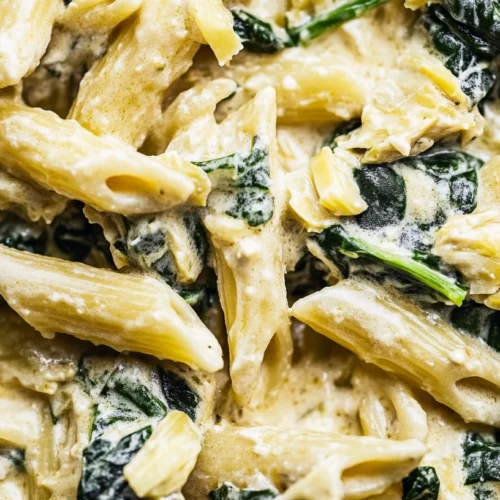 Paleo Pasta: The Best Grain-Free Alternatives & Homemade Recipes 2 Close-up of creamy paleo pasta with spinach and artichoke with dairy-free sauce and wilted spinach leaves.