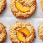 Six golden brown peach upside down cookies on parchment paper, some with caramelized peach slices in the center.